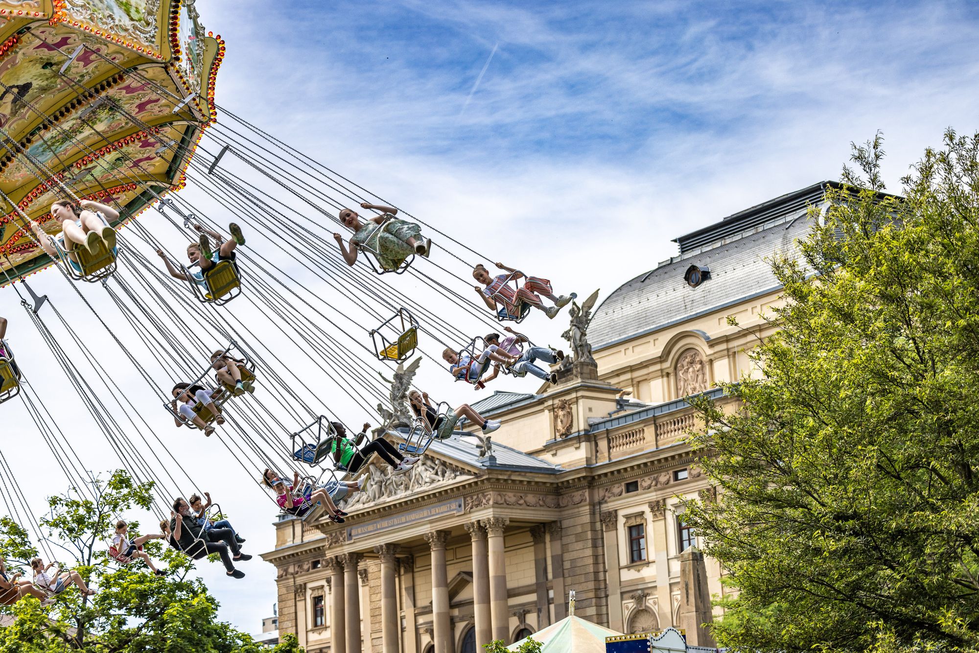 Menschen auf einem Kettenkarussel vor dem Wiesbadener Staatstheater